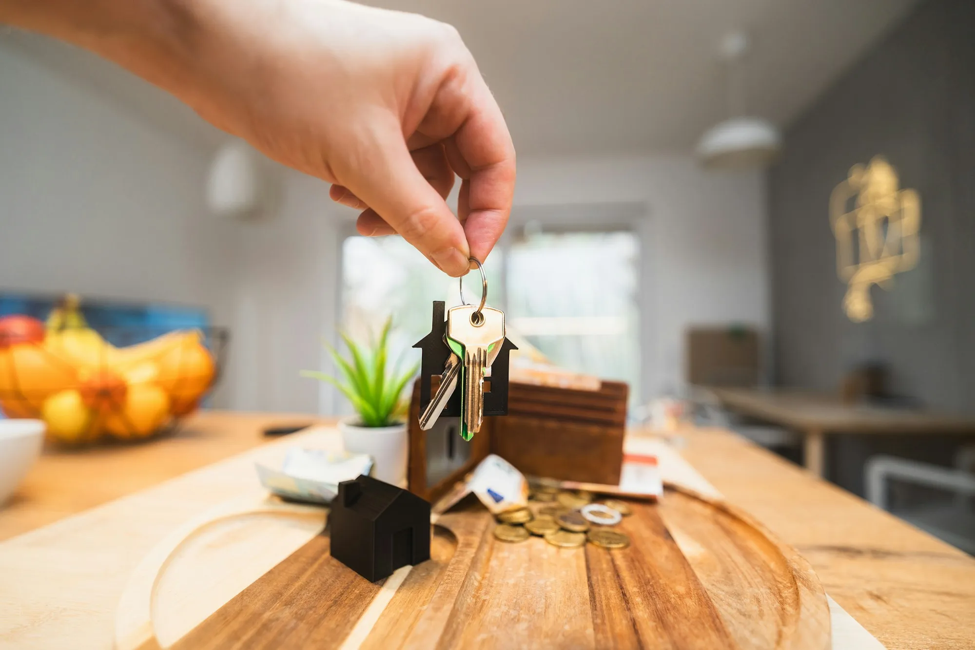 Hand dangling house keys over a small model home on a table