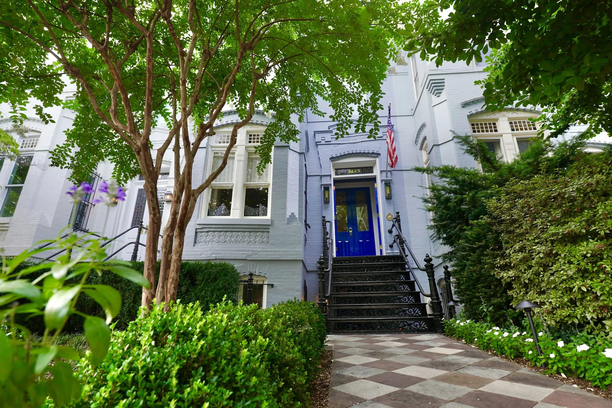 Front steps of a white townhouse framed by trees and garden beds